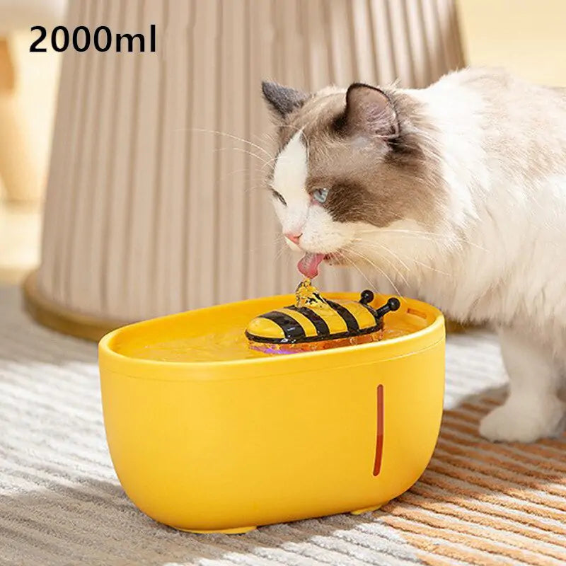 A fluffy cat drinks from a yellow Aqua Pet Stream Fountain by Shopinapets, shaped like a bowl with a floating black and yellow submarine toy. The fountain offers optimal pet hydration with its 2000ml capacity.