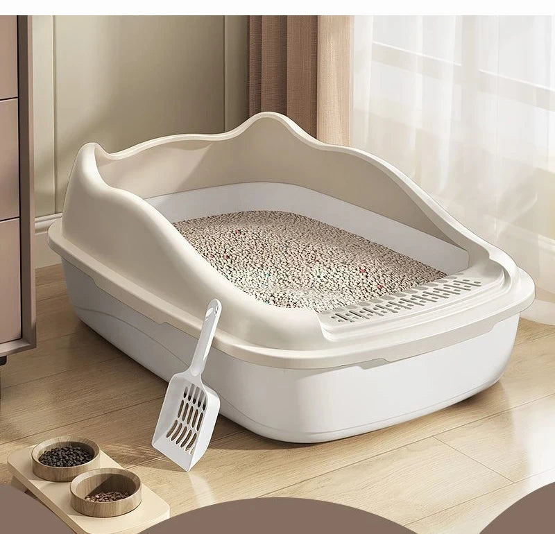A beige cat litter box with a scooper next to it, placed on a wooden floor near a sunny window.