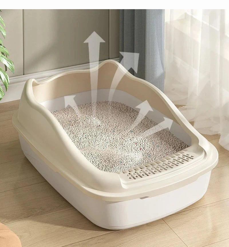A clean cat litter box with a beige rim and granules inside, surrounded by airy curtains and green plants.