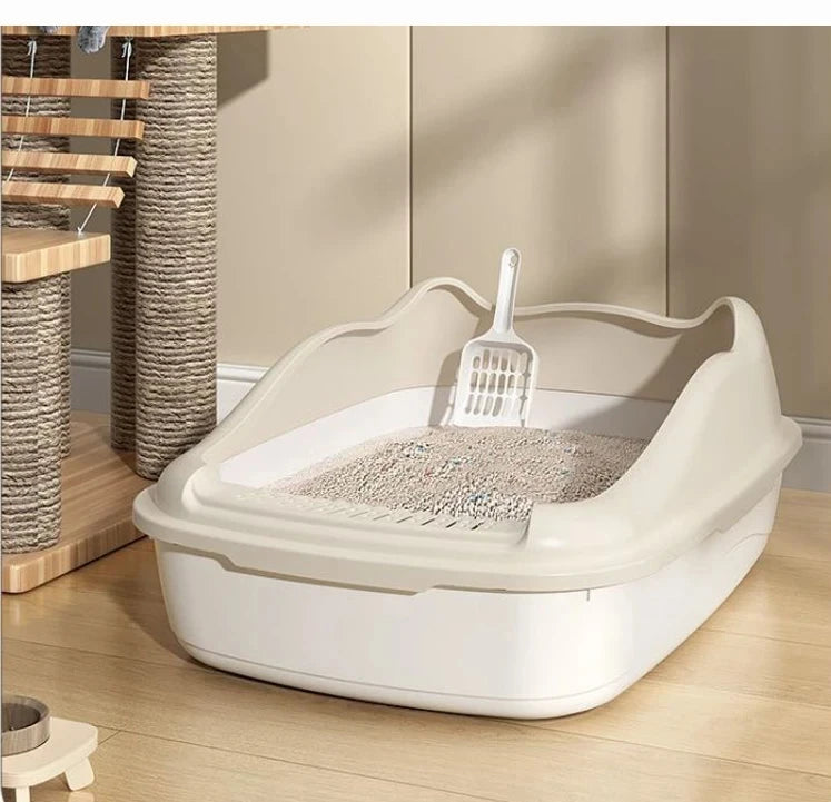 A beige cat litter box with a scoop inside, positioned on wooden flooring near a scratching post and cat tree.
