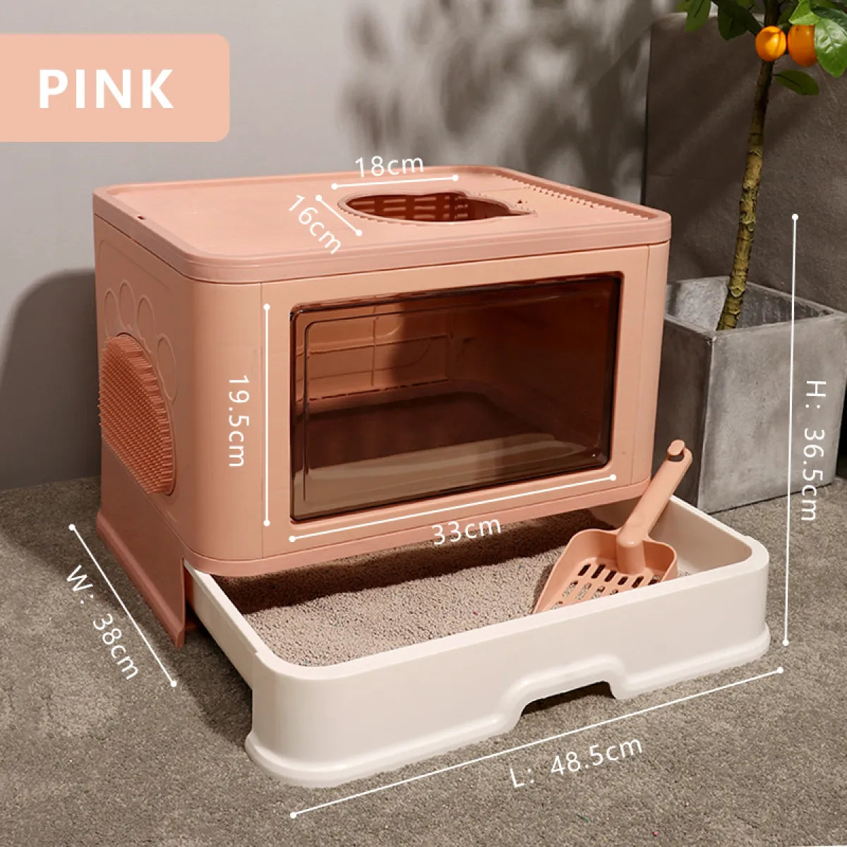 A pink cat litter box with a transparent front, dimensions annotated, and a scoop beside it on a textured gray surface.