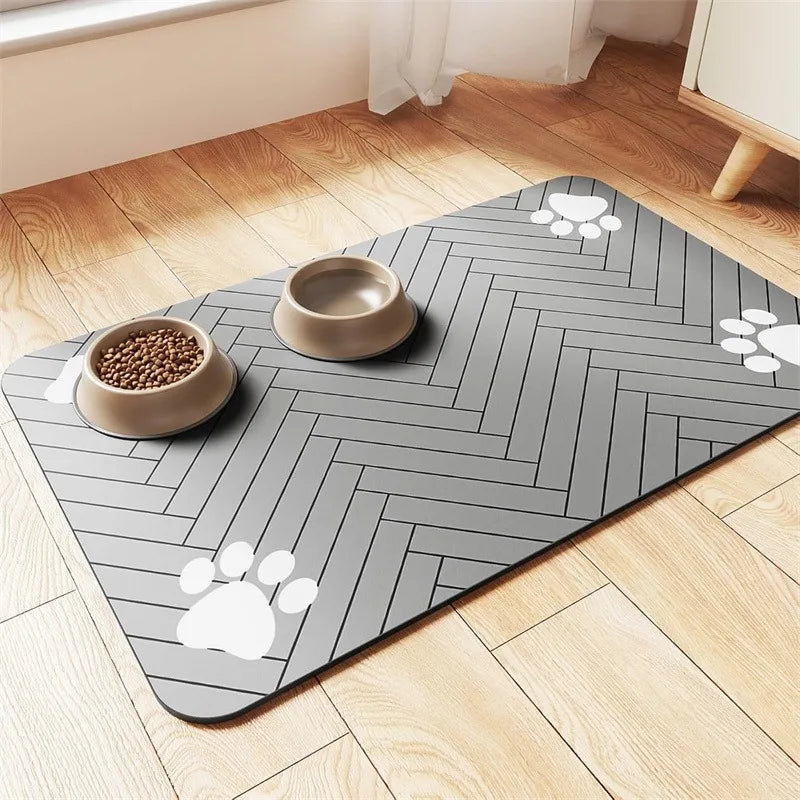 A gray herringbone pet mat with two feeding bowls, one filled with kibble, and white paw prints on the corners.