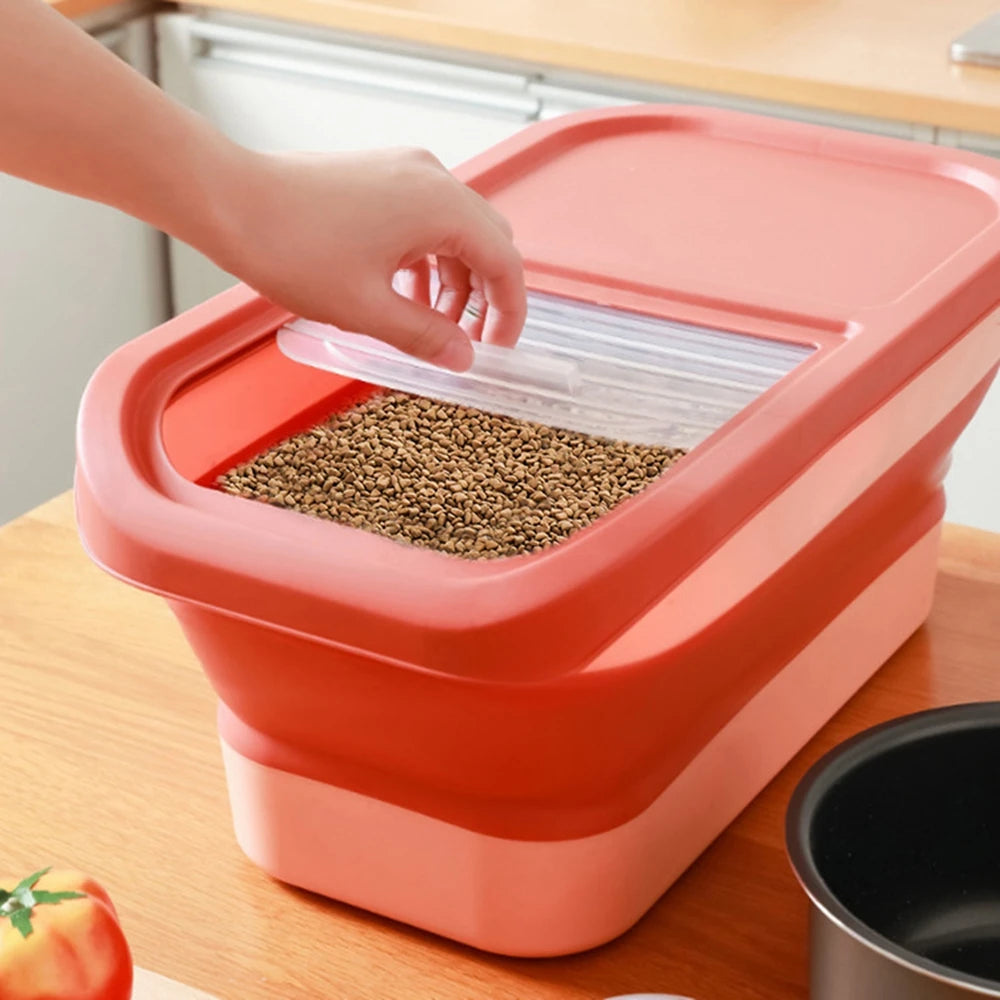 A hand lifts the lid of a large, red food storage container filled with pet dry food, placed on a wooden kitchen countertop.