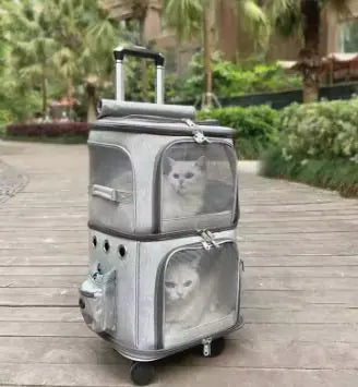 A stylish, gray pet carrier on wheels with two compartments, each housing a curious cat, set on a pathway surrounded by greenery.