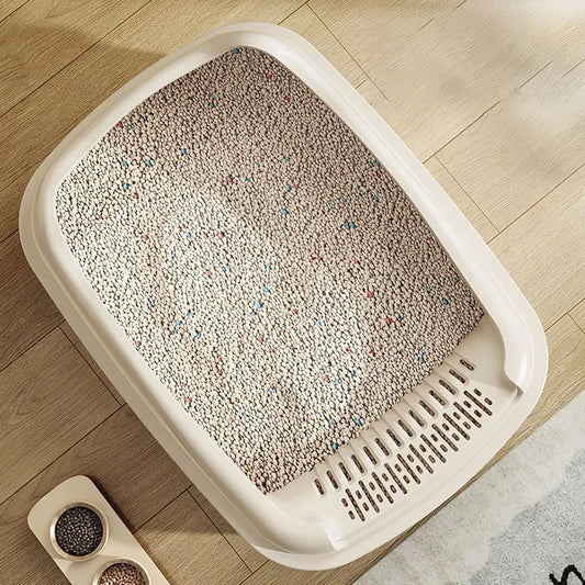 A top view of a cream-colored litter box filled with light-colored, speckled litter, placed on a wooden floor.