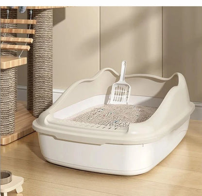 A beige cat litter box with a scoop inside, positioned on wooden flooring near a scratching post and cat tree.