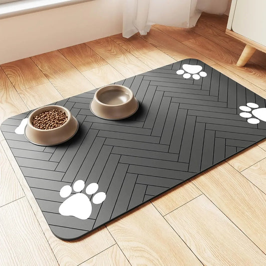 A black pet food mat with a herringbone pattern, featuring two beige bowls for food and water and white paw prints in the corners.
