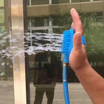 A hand holding a blue water sprayer, directing a spray of water towards a glass surface, with reflections visible in the glass.