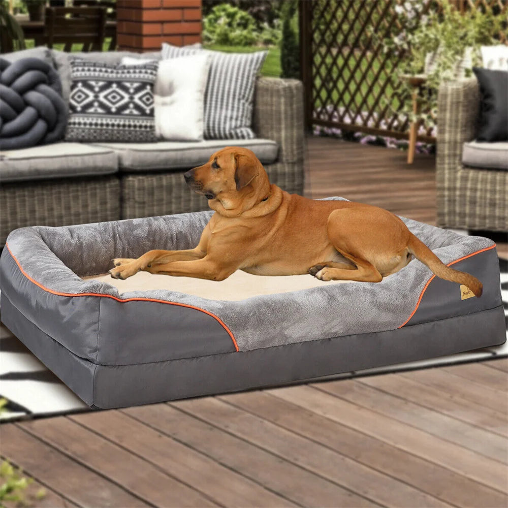Dog lying on a gray pet bed outdoors with a couch and garden in the background