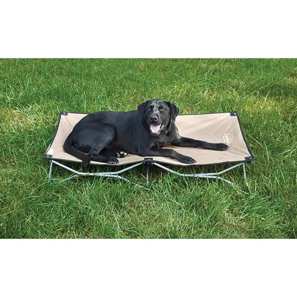 Black dog lying on a beige pet cot in a grassy area